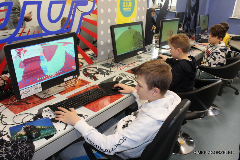 W pomieszczeniu Mediateki przy pięciu stanowiskach komputerowych siedzą chłopcy, tworzący grę komputerową w programie Kodu Game Lab.
