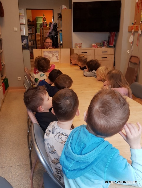 Zajęcia w Miejskiej Bibliotece Publicznej w Zgorzelcu dla grupy przedszkolaków z "Tęczy" o motylach, dzieci słuchają teatrzyka kamishibai.