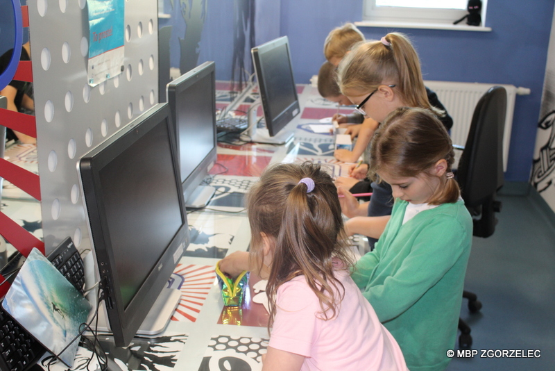 W sali komputerowej Mediateki dzieci kolorują maski dla robotów.