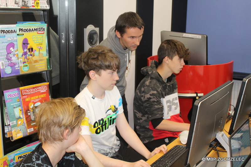 W pomieszczeniu Mediateki bibliotekarz wyjaśnia trzem chłopcom zasady programowania robotów Finch w języku Scratch