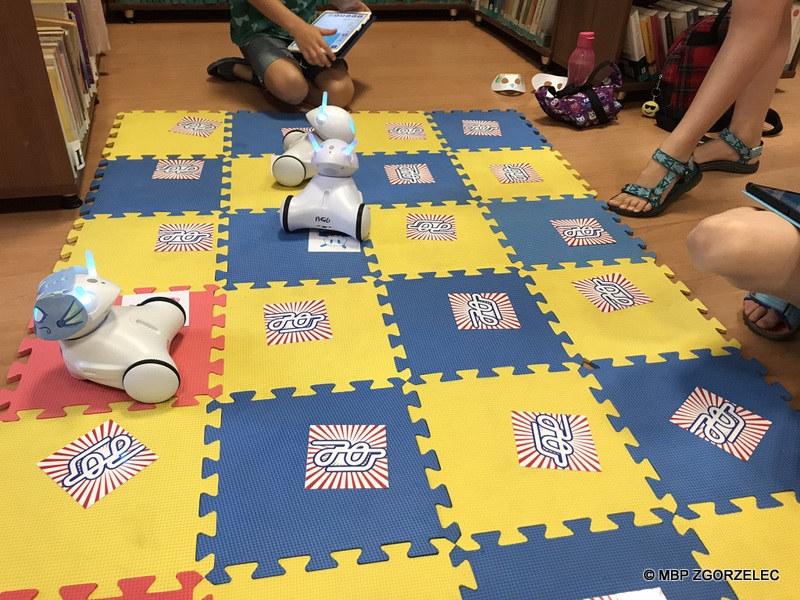 W pomieszczeniu bibliotekipo piankowej macie jeżdżą zaprogramowane roboty. Obok siedzą dzieci i odkrywają wybrane pary kart w grze memory.