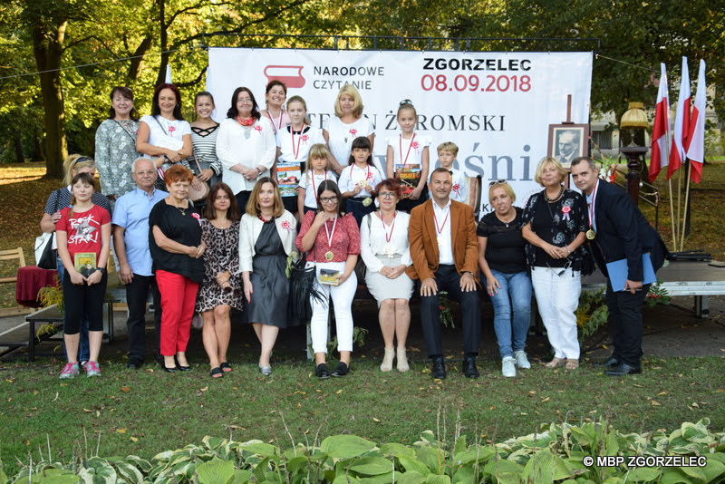 Uczestnicy Narodowego Czytania w Zgorzelcu 2018 pozują do zdjęcia na tle banera Narodowego Czytania. Zdjęcie jest jednocześnie odnośnikiem do wpisu na stronie "Zapraszamy do Narodowego Czytania".