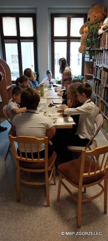 W pomieszczeniu czytelni Oddziału Dla Dzieci i Młodzieży uczniowie klasy 5 ze Szkoły Podstwowej Cogito w Zgorzelcu, ogladają wspólnie wybrane przez siebie książki.