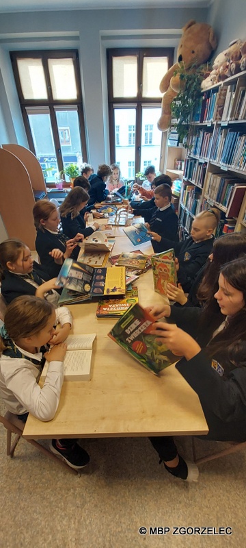 W pomieszczeniu czytelni Oddziału Dla Dzieci i Młodzieży uczniowie klasy 5 ze Szkoły Podstwowej Cogito w Zgorzelcu, ogladają wspólnie interaktywne książki.