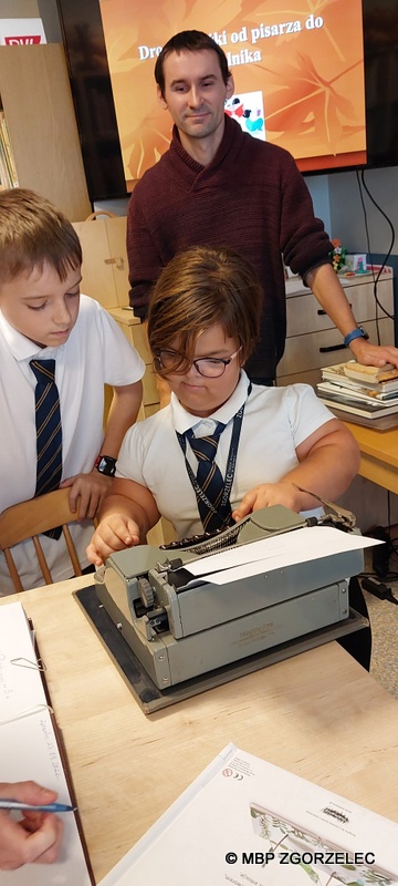 W pomieszczeniu czytelni Oddziału Dla Dzieci i Młodzieży uczniowie klasy 5 ze Szkoły Podstwowej Cogito w Zgorzelcu, piszą na maszynie do pisania.