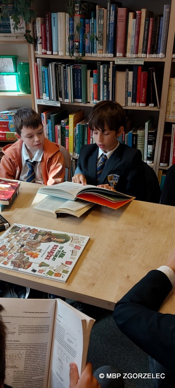 W pomieszczeniu czytelni Oddziału Dla Dzieci i Młodzieży uczniowie klasy 5 ze Szkoły Podstwowej Cogito w Zgorzelcu, ogladają wspólnie wybrane przez siebie książki.