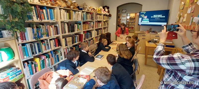 W pomieszczeniu czytelni Oddziału Dla Dzieci i Młodzieży uczniowie klasy 5 ze Szkoły Podstwowej Cogito w Zgorzelcu, ogladają wspólnie teatrzyk Kamishibai prezentowany przez bibliotekarkę.