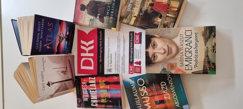 Zbiór ułożonych obok siebie książek z ulotką DKK - dyskusyjnego klubu książki.