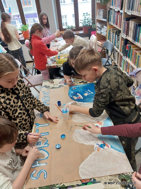 W pomieszczeniu Oddziału Dla Dzieci Miejskiej Biblioteki Publicznej w Zgorzelcu, grupa dzieci wykonuje prace plastyczne.