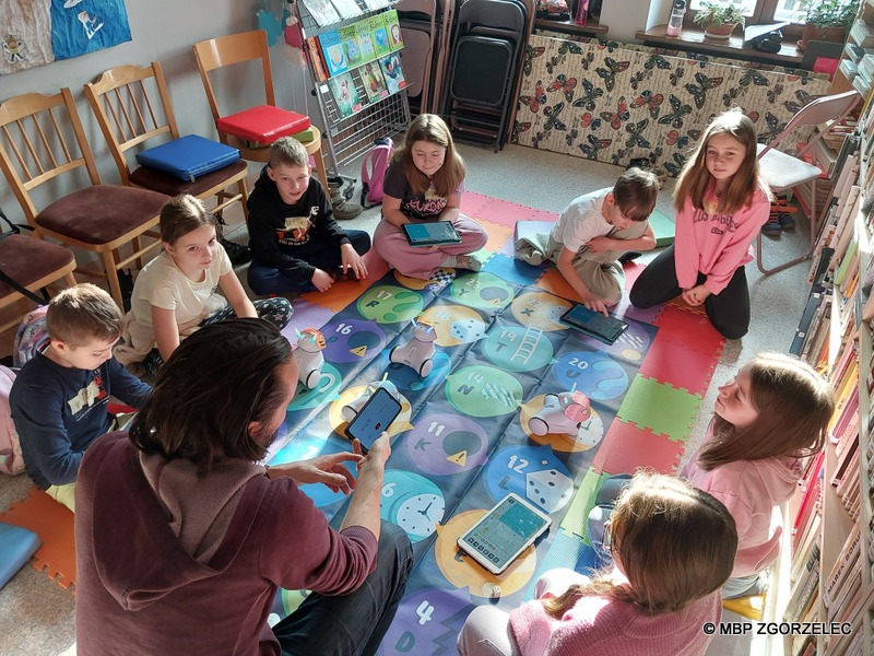 W pomieszczeniu Oddziału Dla Dzieci Miejskiej Biblioteki Publicznej w Zgorzelcu, grupa dzieci programuje roboty