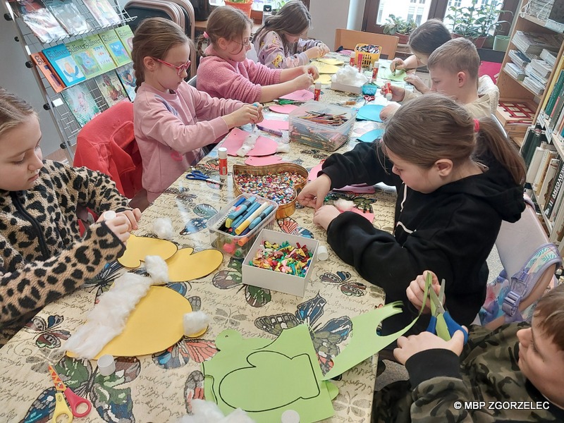 W pomieszczeniu Oddziału Dla Dzieci Miejskiej Biblioteki Publicznej w Zgorzelcu, grupa dzieci wykonuje prace plastyczne.