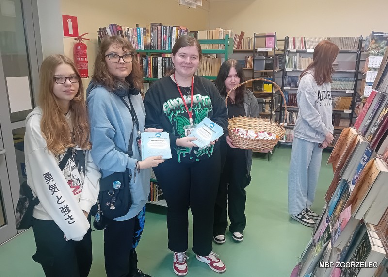 W pomieszczeniu biblioteki szkolnej uczennice przygotowują się do rozdawania rozpuszczalnych gum i ulotek promujących akcję "Książki w chmurach"