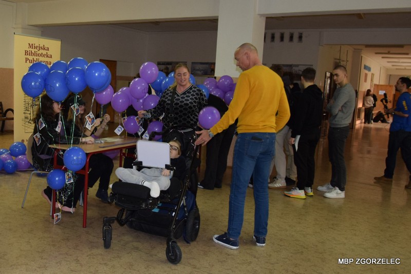 Na korytarzu szkolnym grupa młodzieży stoi w kolejce po odbiór kodów dostępowych do e-podręczników.