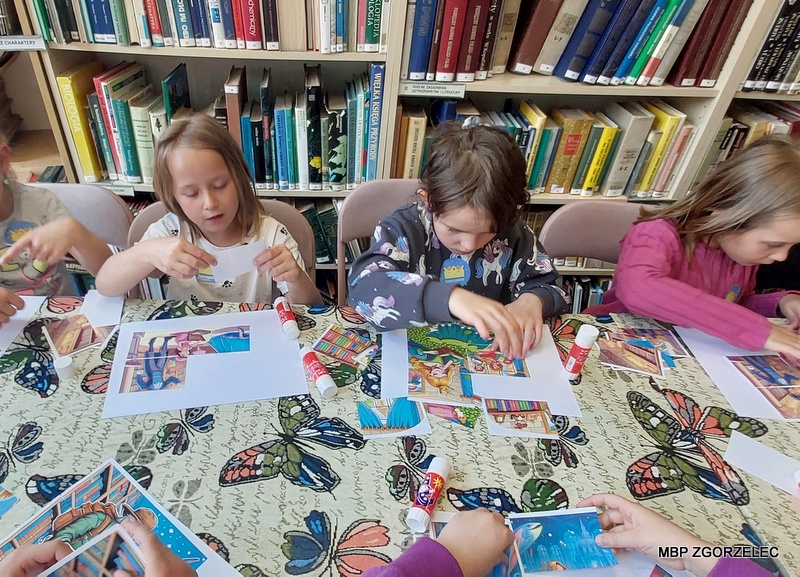 W pomieszczeniu biblioteki grupa dzieci wykonuje prace plastyczne.