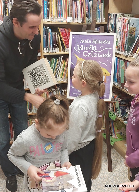 W pomieszczeniu biblioteki, bibliotekarz pasuje na czytelników dzieci.