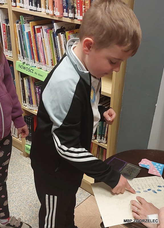 W pomieszczeniu biblioteki, dzieci odbijają odciski swoich palców do kroniki.