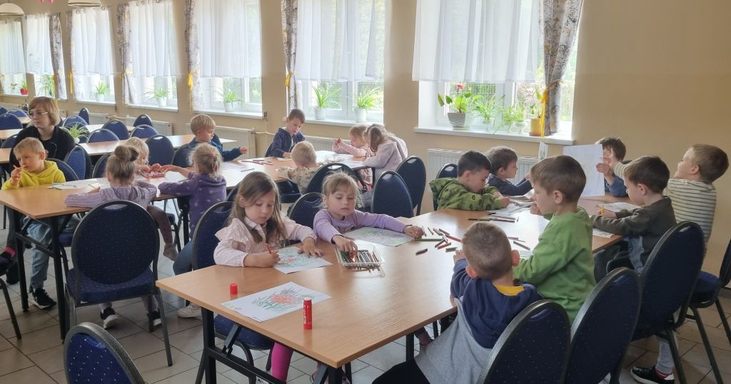 Dzieci wykonują prace plastyczne podczas spotkania w bibliotece.