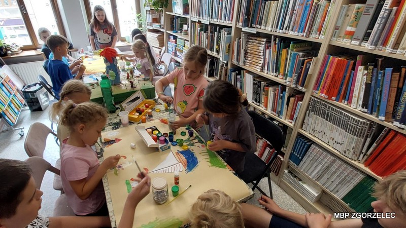 Dzieci malują i rysują przy stole podczas zajęć plastycznych w bibliotece