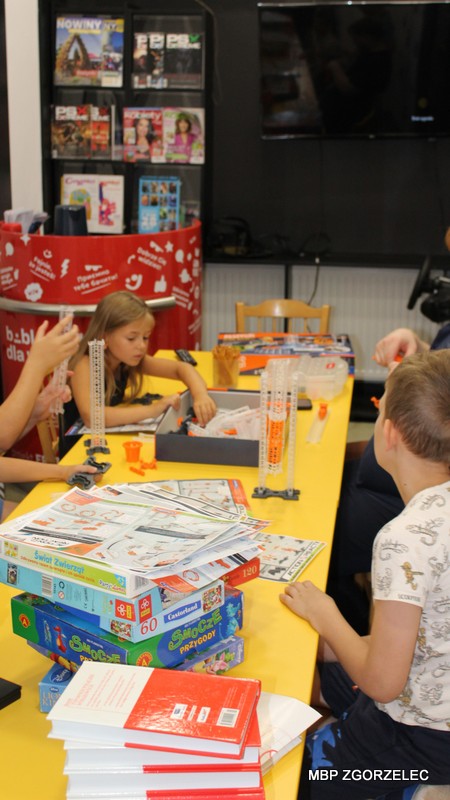 Dzieci bawią się zestawami konstrukcyjnymi przy żółtym stole w Bibliotece Multimedialnej.