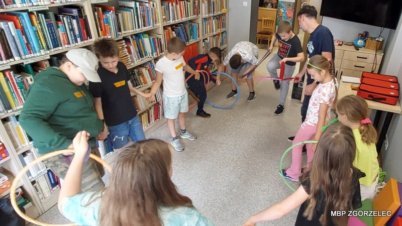 Dzieci z hula-hoopami stoją w kręgu w bibliotece.