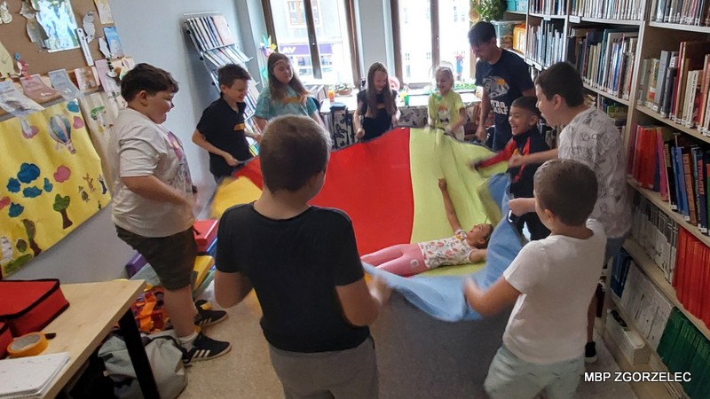 Dzieci bawią się kolorową chustą animacyjną w bibliotece.