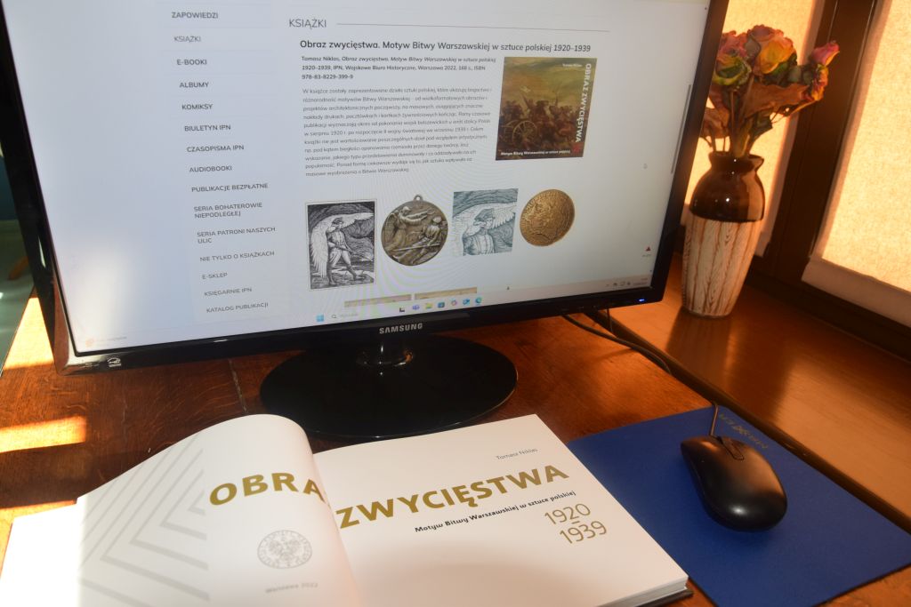 Stanowisko komputerowe w Czytelni MBP. Przed monitorem komputera leży rozłożona książka.