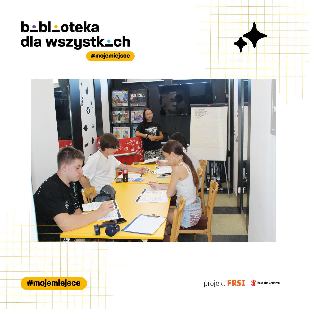 Uczestnicy kursu języka polskiego siedzą przy stole w bibliotece, otoczeni książkami i materiałami edukacyjnymi. Na zdjęciu znajduje się tekst: „biblioteka dla wszystkich #mojemiejsce, projekt FRSI Save the Children.