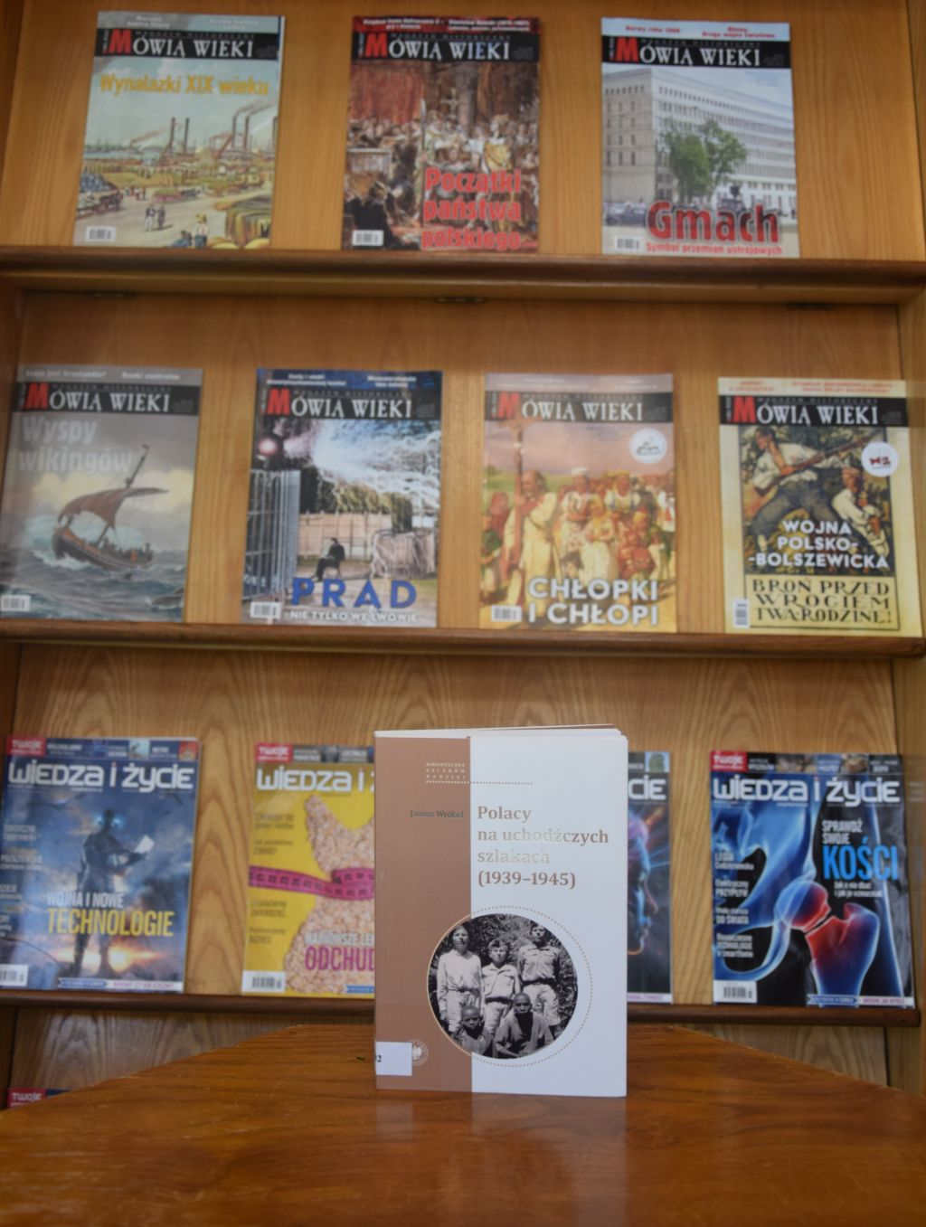 Książka Janusza Wróbla „Polacy na uchodźczych szlakach (1939-1945)” na tle czasopism w Czytelni MBP. Zdjęcie jest odnośnikiem do wpisu o książce.