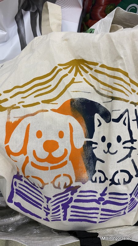 Zbliżenie na ekologiczną torbę ozdobioną kolorowym nadrukiem przedstawiającym uśmiechniętego psa i&nbsp;kota siedzących razem w&nbsp;budzie z&nbsp;dachem w&nbsp;kształcie otwartej książki