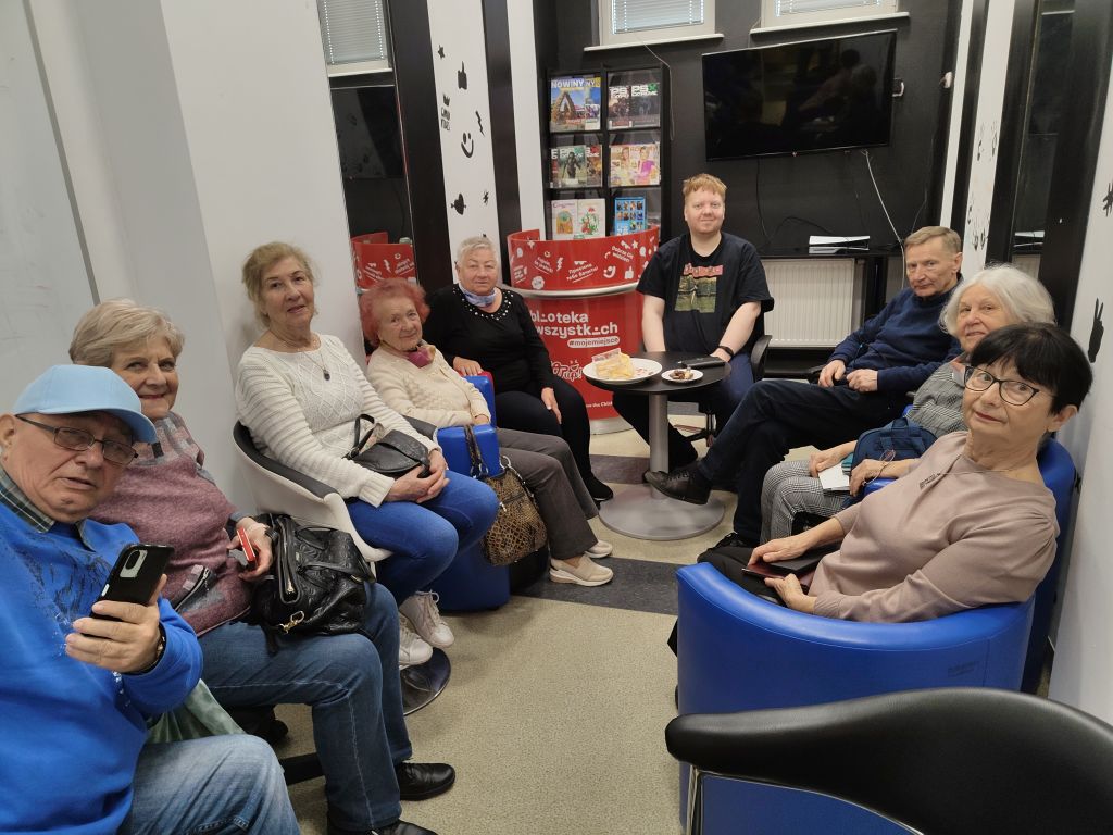 Uczestnicy zajęć edukacji cyfrowej dla seniorów pozują do wspólnego zdjęcia razem z bibliotekarzem prowadzącym zajęcia w Filii nr 1 przy ul. Orzeszkowej 30a. Zdjęcie jest odnośnikiem do wpisu "Zajęcia edukacji cyfrowej".