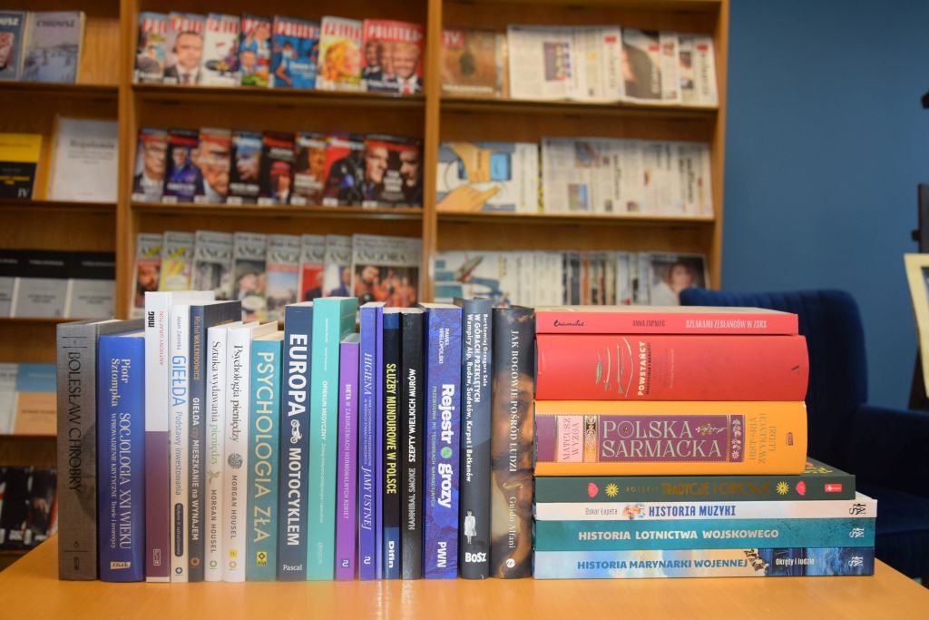 Nowe książki w Czytelni MBP na tle regałów z czasopismami. Zdjęcie jest odnośnikiem do wpisu "Nowe książki w Czytelni MBP".