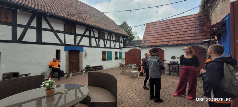Dziedziniec gospodarstwa agroturystycznego z&nbsp;zabudową o&nbsp;charakterze historycznym; uczestnicy rajdu rowerowego rozmawiają i&nbsp;odpoczywają podczas postoju.