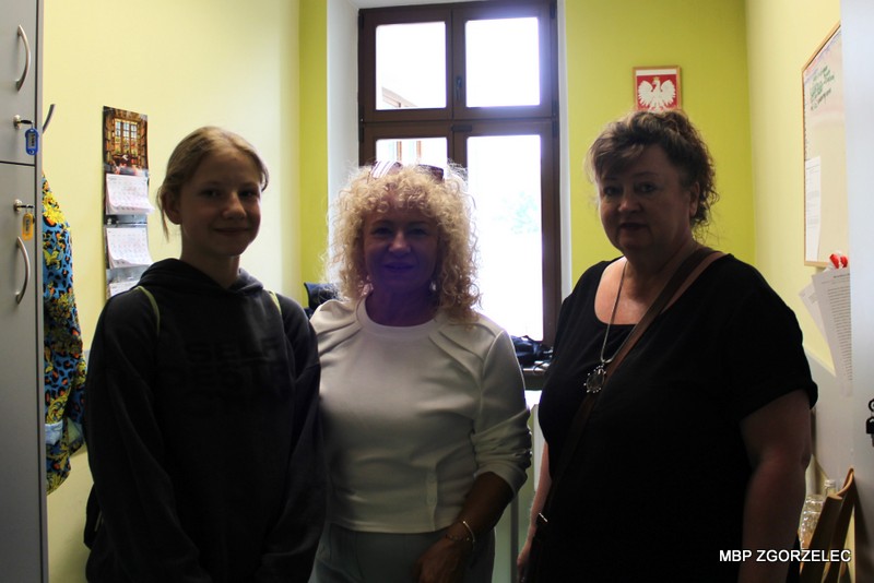 Dyrekcja MBP Zgorzelec oraz wychowaczyni klasy 6c z&nbsp;uczennicą pozują do zdjęcia we wnętrzu pomieszczenia księgowości i&nbsp;administracji na tle okna. W&nbsp;pomieszczeniu widoczne są elementy wyposażenia biurowego oraz jasne ściany.
