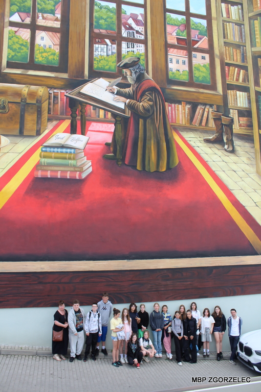 Na ścianie kamienicy widoczny jest duży mural przedstawiający Jakuba Boehme piszącego przy pulpicie w&nbsp;otoczeniu książek. Na dole, pod muralem, stoi grupa uczniów podczas wizyty w&nbsp;bibliotece.