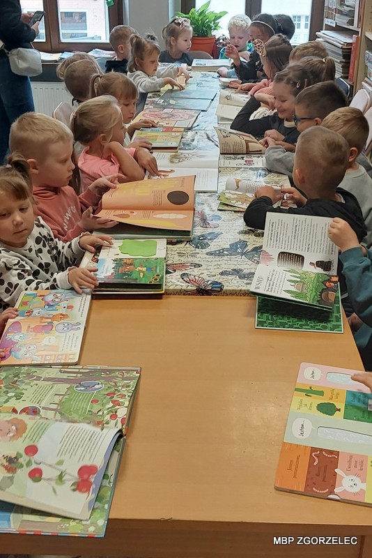 Przedszkolaki podczas wizyty w&nbsp;Oddziale dla Dzieci i&nbsp;Młodzieży przeglądają książki o&nbsp;warzywach zgromadzone na wspólnym stole.