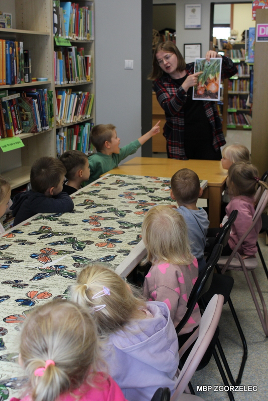 Uczestnicy wrześniowej wizyty w&nbsp;bibliotece zapoznają się z&nbsp;ilustracjami przedstawiających warzywa.