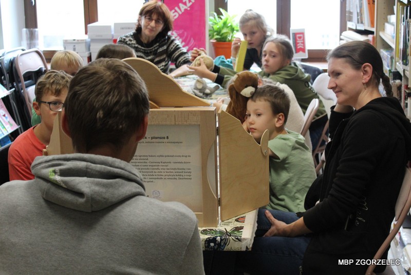 Dzieci uczestniczą w&nbsp;warsztatach plastycznych i&nbsp;przygotowują kartonowe teatrzyki inspirowane baśnią „Czerwony Kapturek”. Na stole znajdują się pudełka, kolorowy papier, nożyczki i&nbsp;materiały plastyczne.